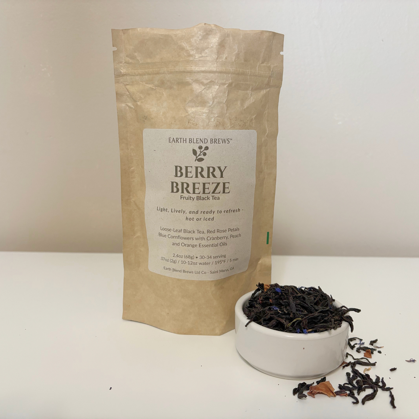 Bag of Earth Blend Brews Berry Breeze tea with a small bowl of tea leaves on a white background