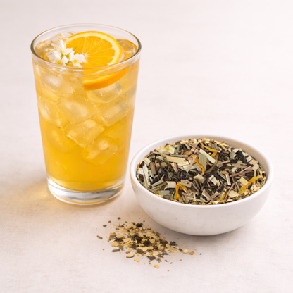 Glass of iced tea with orange slices next to a bowl of tea leaves on a light background