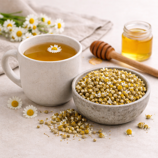 Cup of chamomile tea with a bowl of dried chamomile flowers and a jar of honey on a light background.