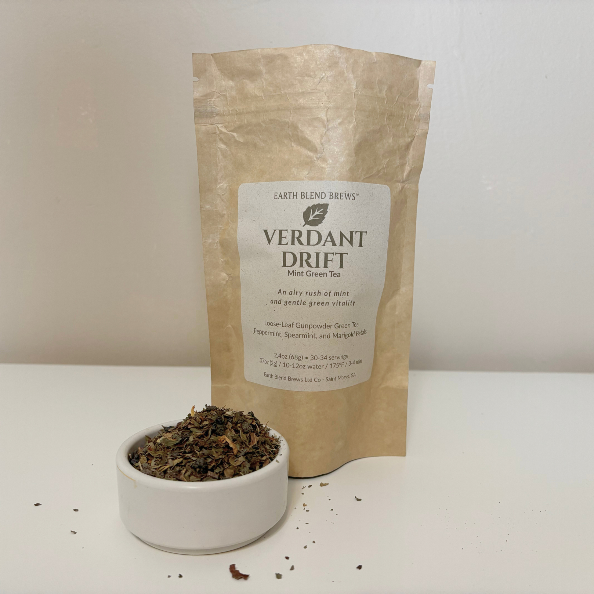 Tea packaging with a label 'VERDANT  DRIFT' and a bowl of tea leaves on a white background